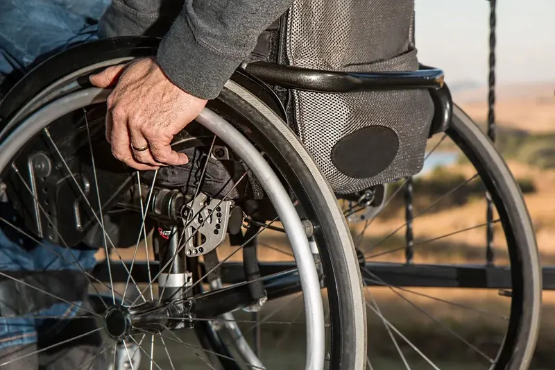 Close-up of a hand gripping the push rim of a manual wheelchair on an outdoor path near Lake Worth, FL